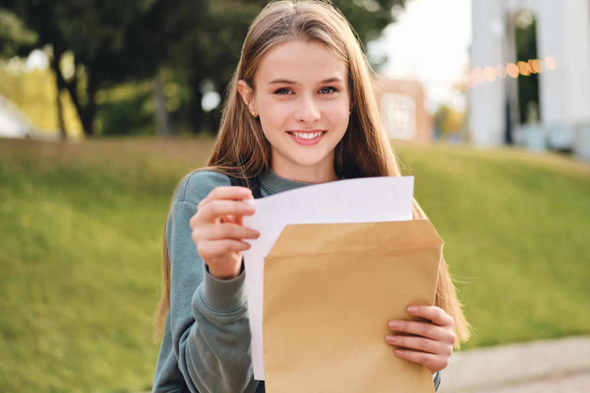 beautiful-cheerful-casual-student-girl-opening-envelope-with-exams-results-happily-looking-in-camera-in-city-park.jpg